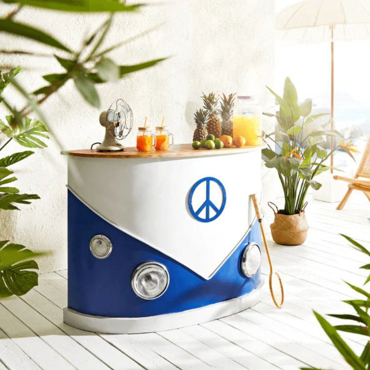 A camper van-themed bar counter with a blue and white color scheme, featuring headlights and a peace symbol emblem, set in a tropical-style