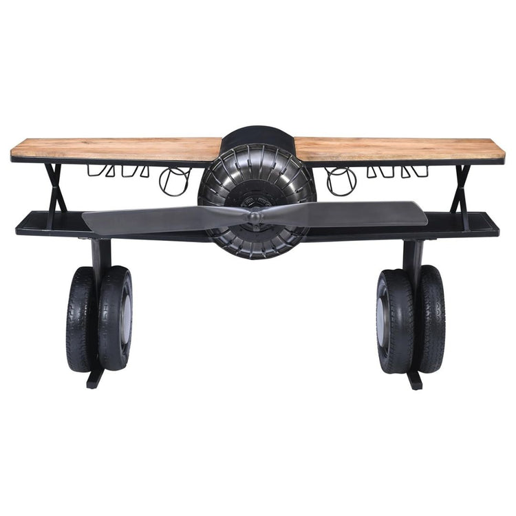 Industrial airplane-engine style bar cart with propeller decoration and dual shelves, featuring wooden tabletop, black metal frame, large rubberized wheels, hanging wine-glass rack and storage for bottles, set in a modern living-room environment