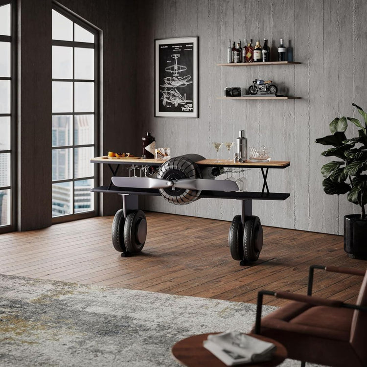 Industrial airplane-engine style bar cart with propeller decoration and dual shelves, featuring wooden tabletop, black metal frame, large rubberized wheels, hanging wine-glass rack and storage for bottles, set in a modern living-room environment