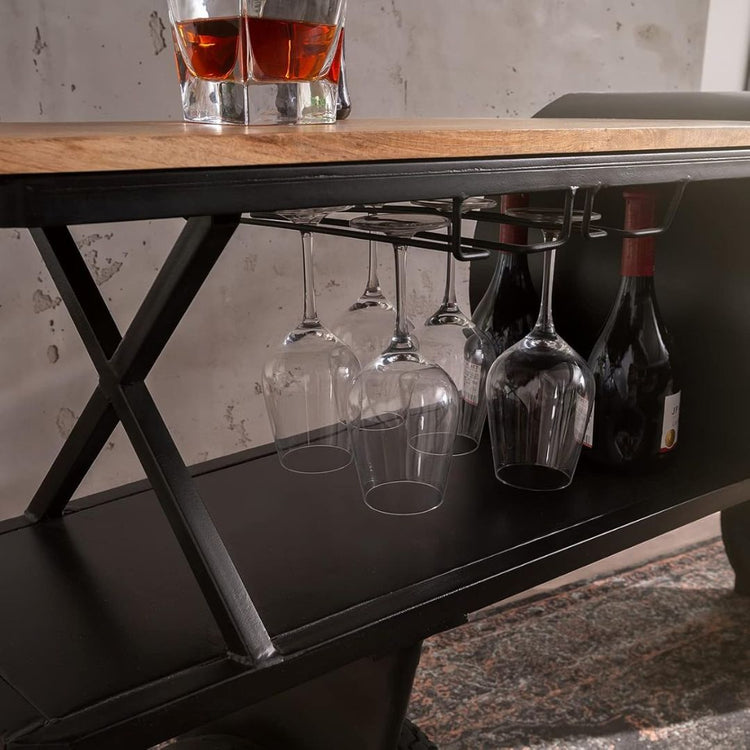 Industrial airplane-engine style bar cart with propeller decoration and dual shelves, featuring wooden tabletop, black metal frame, large rubberized wheels, hanging wine-glass rack and storage for bottles, set in a modern living-room environment