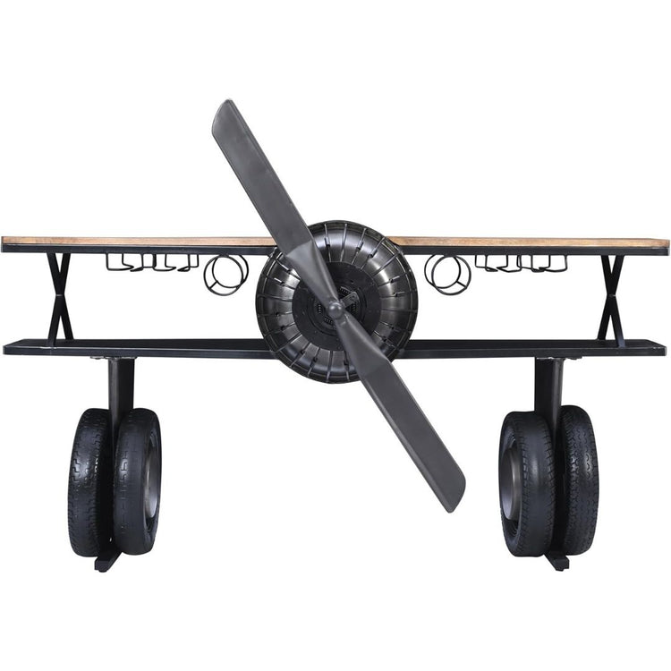 Industrial airplane-engine style bar cart with propeller decoration and dual shelves, featuring wooden tabletop, black metal frame, large rubberized wheels, hanging wine-glass rack and storage for bottles, set in a modern living-room environment