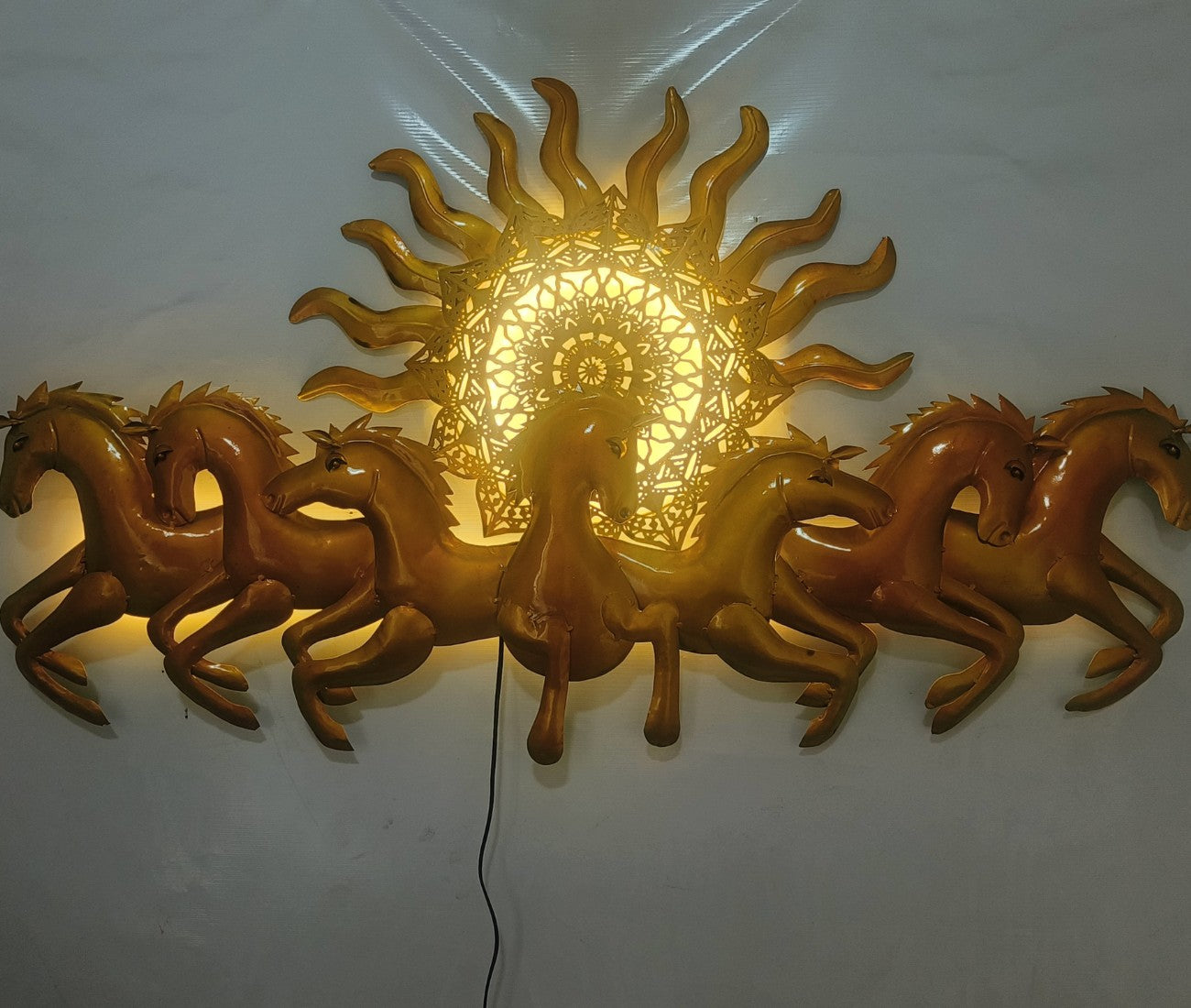 This Designer Gold metal wall art features a stunning depiction of 7 galloping horses against a warm sun backdrop. At 48 x 28 inches, it is sure to make a statement in any room. The integrated LED lights add a touch of modernity and ambiance. Perfect for any equestrian enthusiast.  Size: 48 x 28 Inches.  Made of High-Quality Iron Metal Anti-rust powder coating used for long lasting finish Hanging Mechanism included Horse wall decor with led lighting Perfect for your living room, bedroom, hall, office recept