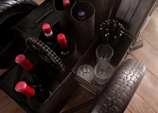 Bar cart with wine bottles, glasses, and cocktail shakers on a wooden floor.