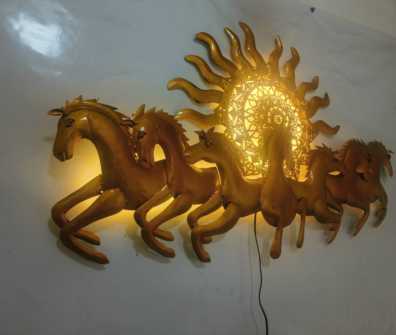 This Designer Gold metal wall art features a stunning depiction of 7 galloping horses against a warm sun backdrop. At 48 x 28 inches, it is sure to make a statement in any room. The integrated LED lights add a touch of modernity and ambiance. Perfect for any equestrian enthusiast.  Size: 48 x 28 Inches.  Made of High-Quality Iron Metal Anti-rust powder coating used for long lasting finish Hanging Mechanism included Horse wall decor with led lighting Perfect for your living room, bedroom, hall, office recept