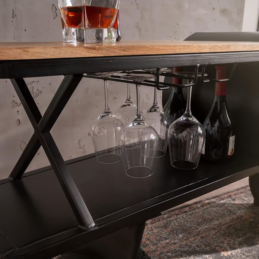 Industrial airplane-engine style bar cart with propeller decoration and dual shelves, featuring wooden tabletop, black metal frame, large rubberized wheels, hanging wine-glass rack and storage for bottles, set in a modern living-room environment