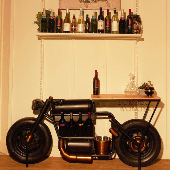 A bar table with a vintage motorcycle design, featuring a wooden tabletop, built-in wine rack, and glass holders. The table is styled with a black and gold finish and has a realistic motorcycle frame as a decorative element.